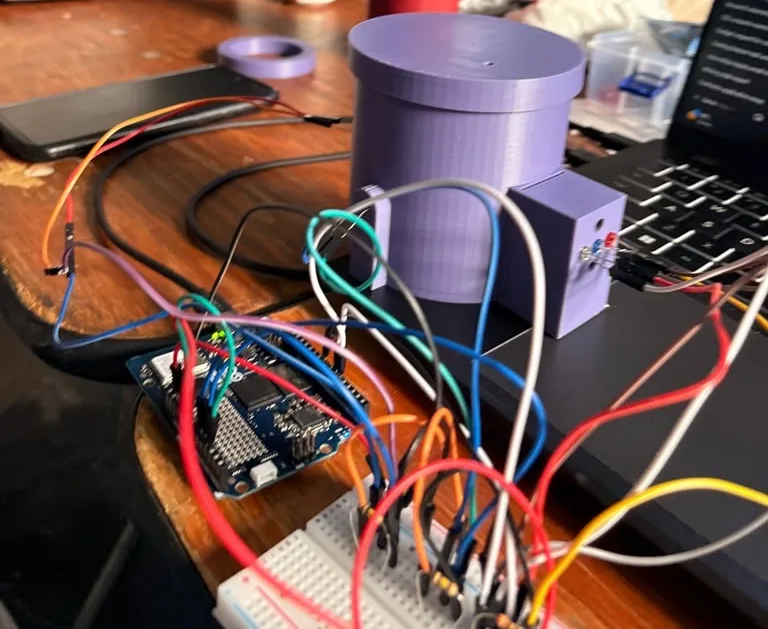The whole station on a table: the purple chamber with its lid, the LED box with its three LEDs, the Arduino UNO Q, a breadboard covered in jumper wires, and a spare purple cup shim ring at the back