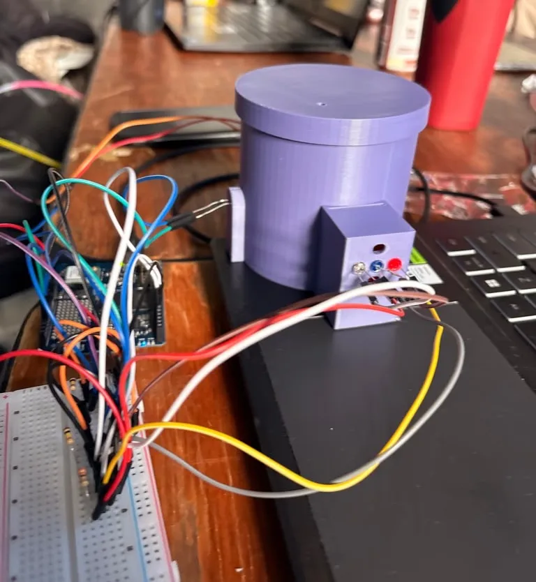 The station with its flat purple lid on, a small hole in the lid, the LED box facing the camera, a photoresistor holder on the left wall with two wires, and a breadboard with resistors and jumper wires in front